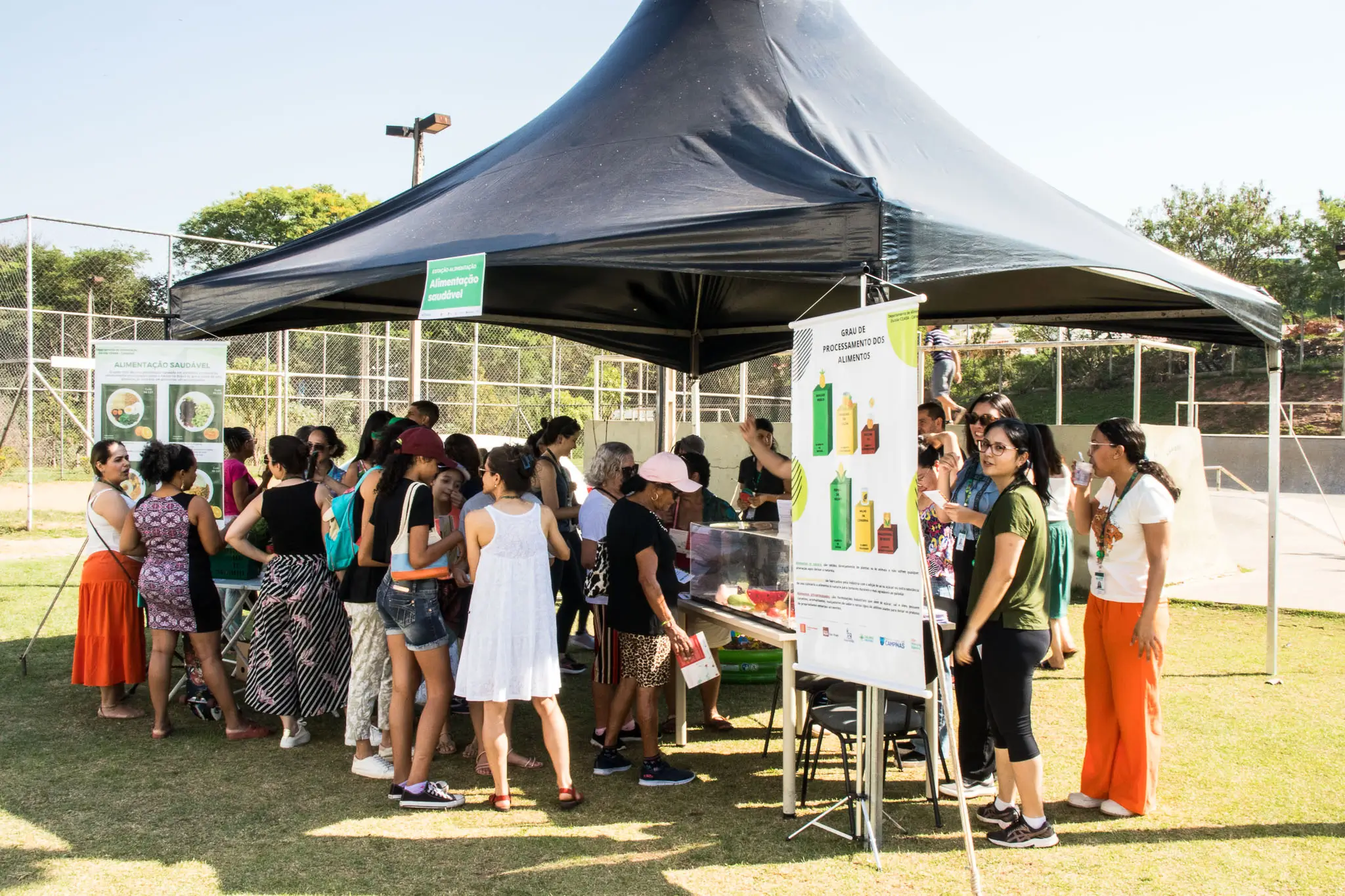 Grupo numeroso de participantes de uma ação comunitária posa junto em um espaço aberto, entre jalecos, camisetas coloridas e balões prateados ao fundo